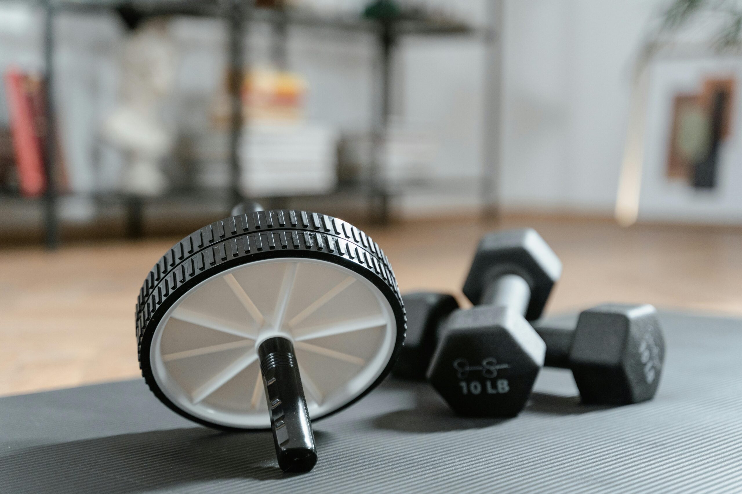 Ab roller and dumbbells on yoga mat, perfect for a home workout routine and healthy lifestyle.